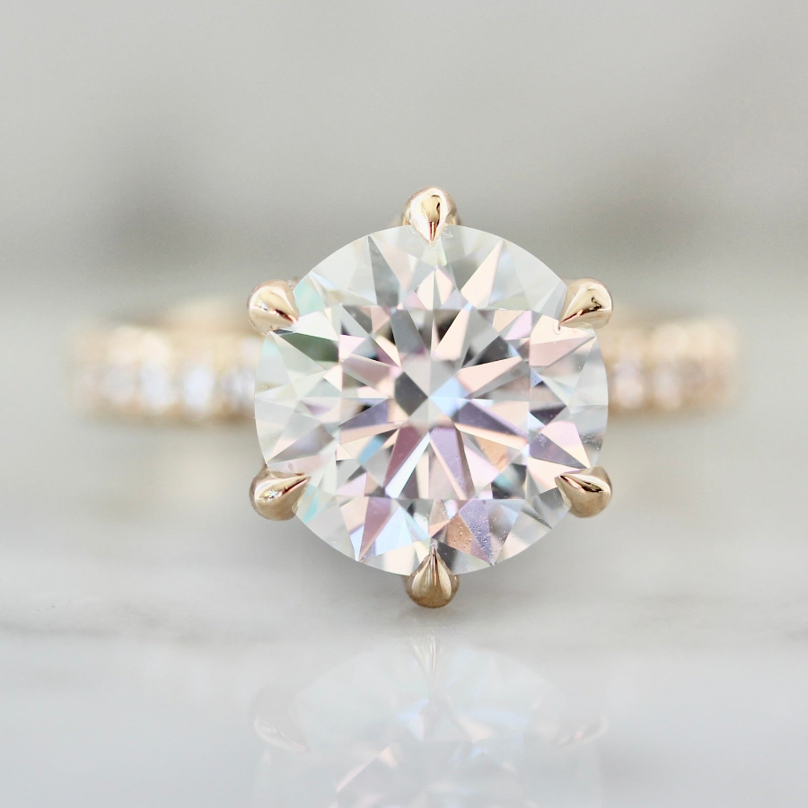 Solitaire round cut diamond engagement ring with six-prong setting and pavé diamond band in peach gold by Gem Breakfast
