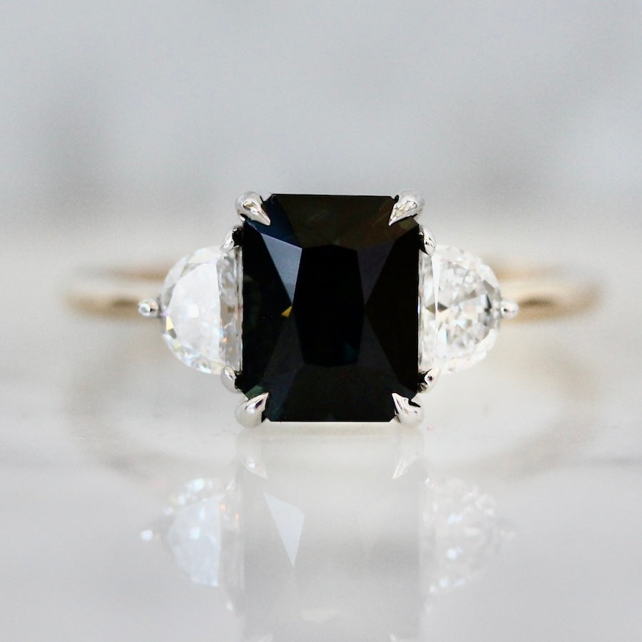 Custom radiant cut deep blue sapphire engagement ring with half moon diamond side stones by Gem Breakfast