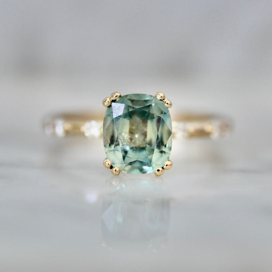 Custom engagement ring with light green cushion cut sapphire and diamond accent stones by Gem Breakfast