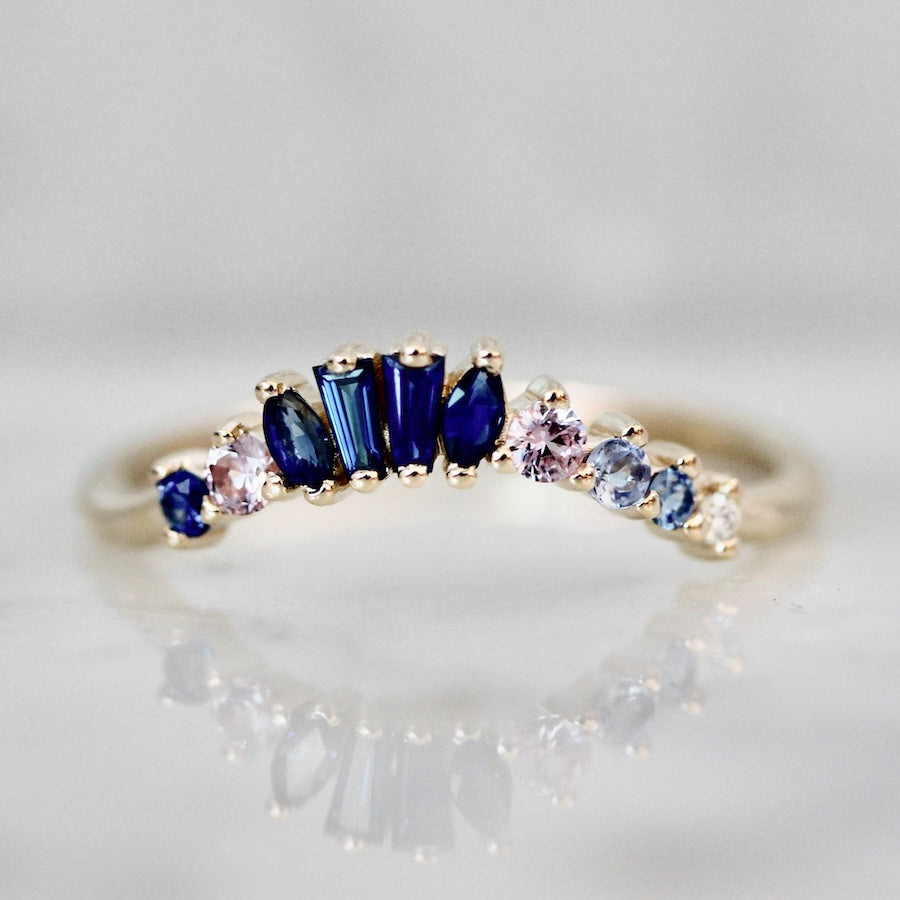 Custom curved wedding band with mixed-cut dark and light blue sapphires by Gem Breakfast