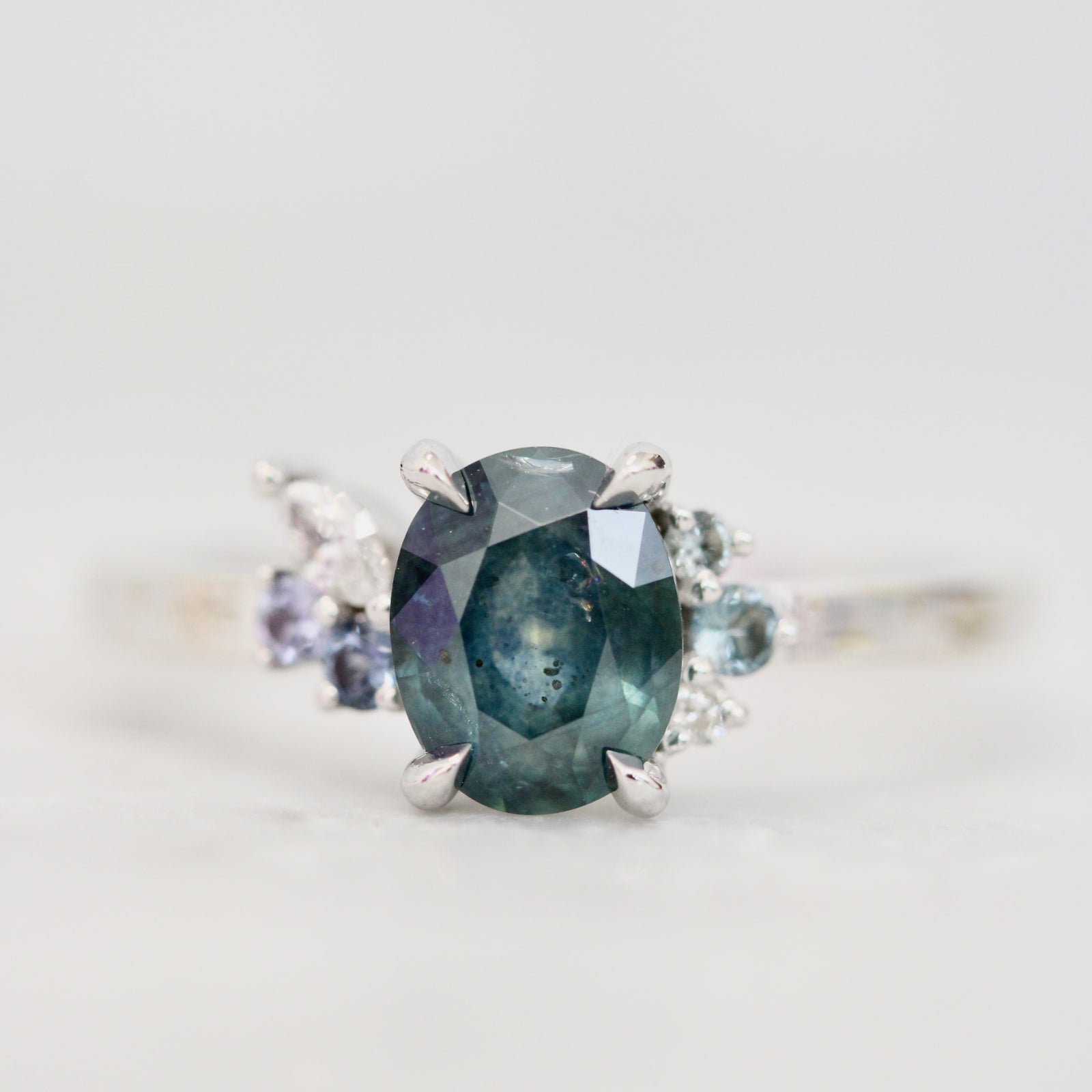 Oval cut green sapphire engagement ring with asymmetrical accents in a white gold custom setting by Gem Breakfast