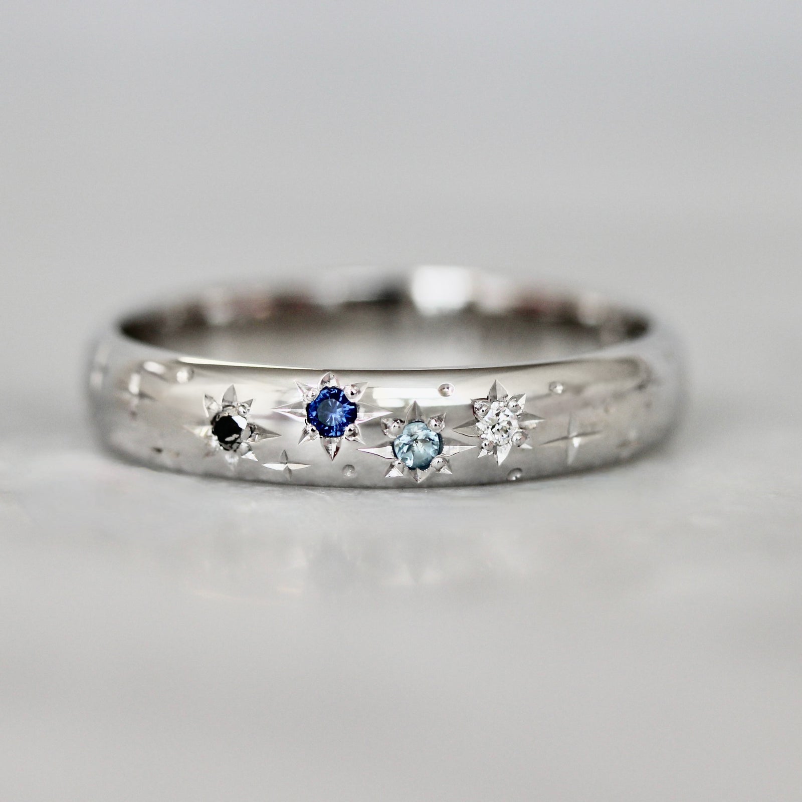 4mm white gold custom wedding band with hand-engraved stars and star-set black diamonds, white diamonds, sapphire, and aquamarine by Gem Breakfast