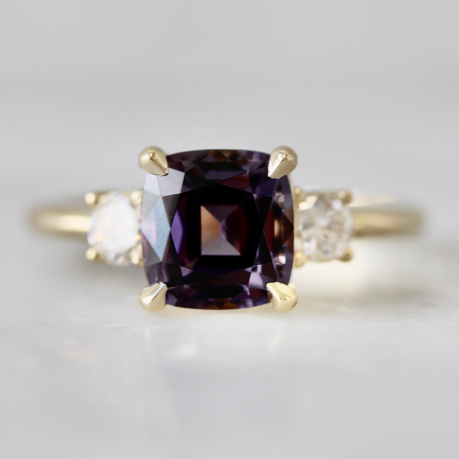 Purple cushion cut spinel three stone custom engagement ring with round brilliant diamond accents by Gem Breakfast