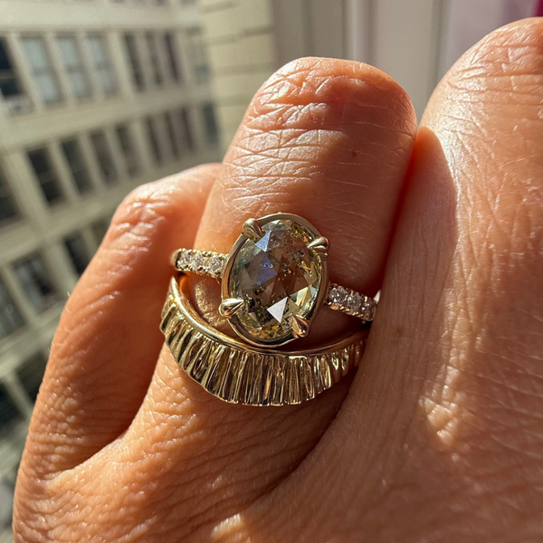 A yellow gold ring featuring an oval-cut, faceted champagne-colored gemstone in a prong setting, with small clear accent stones along the shoulders, shown on a light gray background.