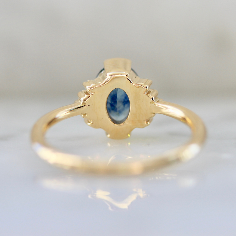 blue oval cut sapphire ring in half bezel with white baguette half halo in yellow gold