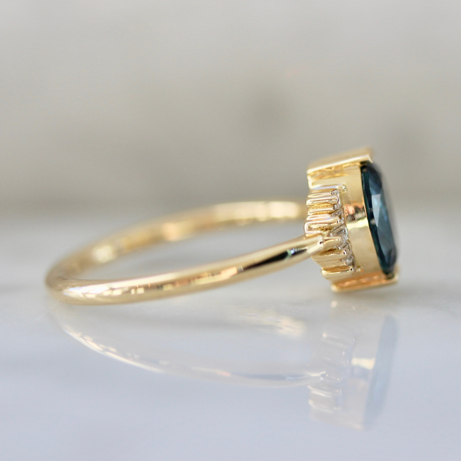
            blue oval cut sapphire ring in half bezel with white baguette half halo in yellow gold